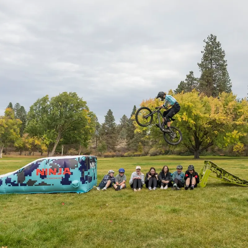 Rider jumping off a lime Ninja ramp over a row of kids onto a Ninja airbag lander